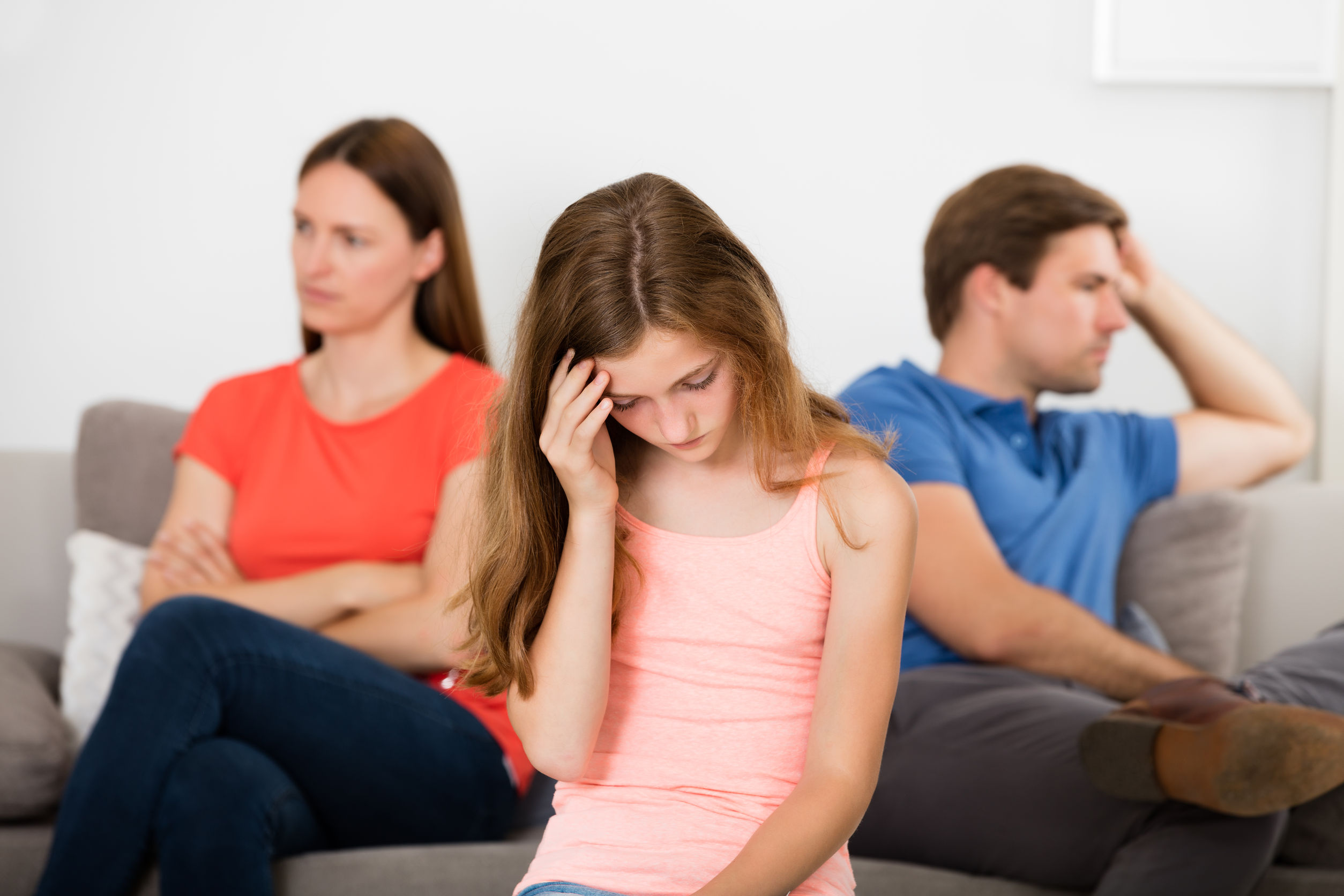 63937562 - upset girl in front of her unhappy parent sitting on sofa